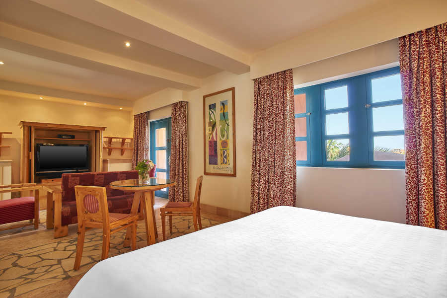 The junior suite of Sheraton Miramar El Gouna furnished with luxury king bedding and living area with dinning table and sofa
