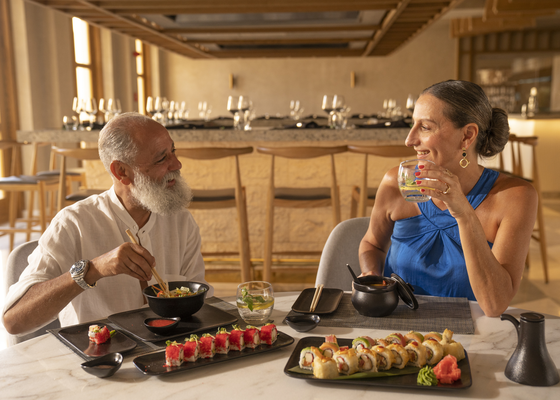 a man and a woman having dinner at harumaki at steigenberger el gouna. They are both eating sushi and the woman is holding a drink