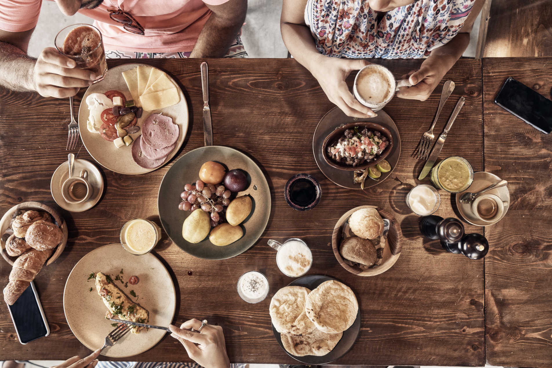 Top view for Cook's Club breakfast showing food plates and fruit basket with juices and coffee above wooden table in El Gouna