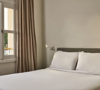 Captain's Inn Standard Room with biege walls a King size bed and a courtyard view on the pleasant greenery from the window