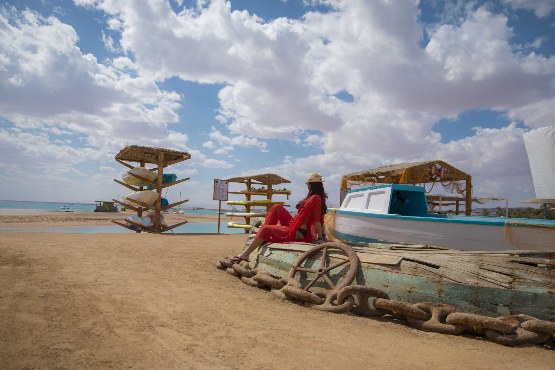 A girl is sitting on a vintage boat at Club Paradisio Sandy Beach and the sky is full of clouds in El Gouna 4 Stars Hotel