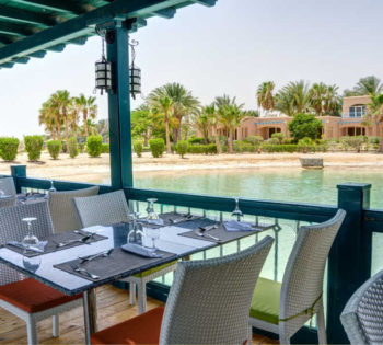 Dining tables of Marco Polo Restaurant surrounded by Red Sea lagoons and greenish landscape at Club Paradisio El Gouna Hotel