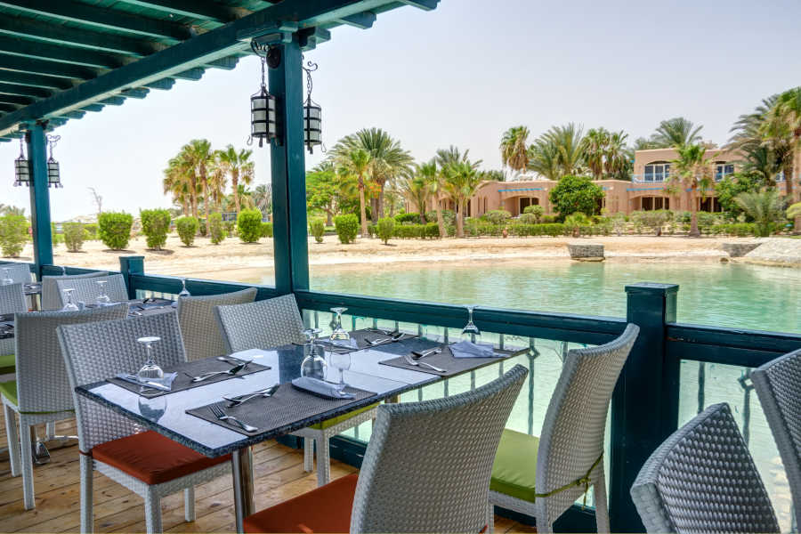 Dining tables of Marco Polo Restaurant surrounded by Red Sea lagoons and greenish landscape at Club Paradisio El Gouna Hotel