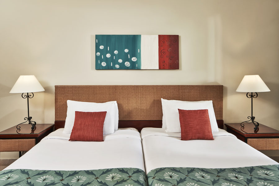 2 twins bed of Fanadir Hotel in El Gouna with 2 side tables and 2 chandelier at the accessible rooms with orange green theme