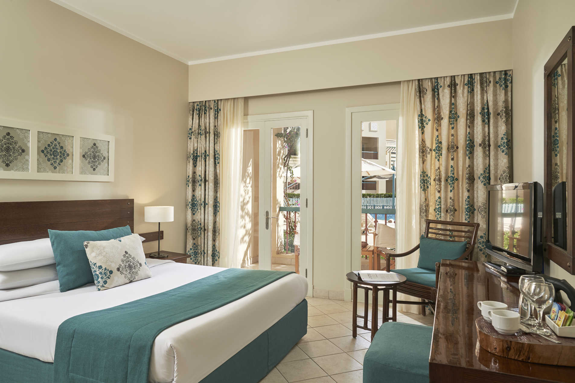 The king bed room in Mosaique Hotel El Gouna with turqouise touch and small coffee table with a window to the room terrace