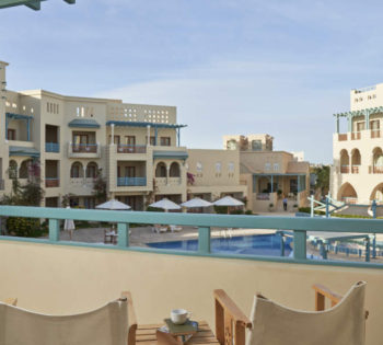 The pool view from standard room balcony with a small table for coffee and 2 chairs at Mosaique El Gouna Hotel