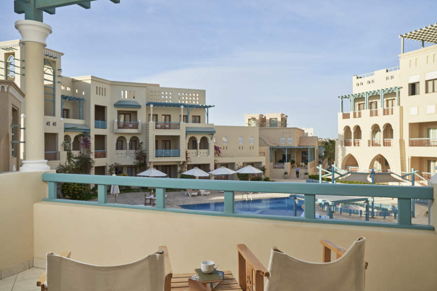 The pool view from standard room balcony with a small table for coffee and 2 chairs at Mosaique El Gouna Hotel