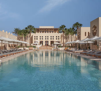 hotel swimming pool with long chairs and umbrellas and steigenberger hotel in background with palm trees