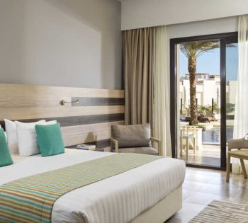 The king sized bedroom at Ancient Sands Resort El Gouna with a glass door to the pool and a beige theme for the decoration