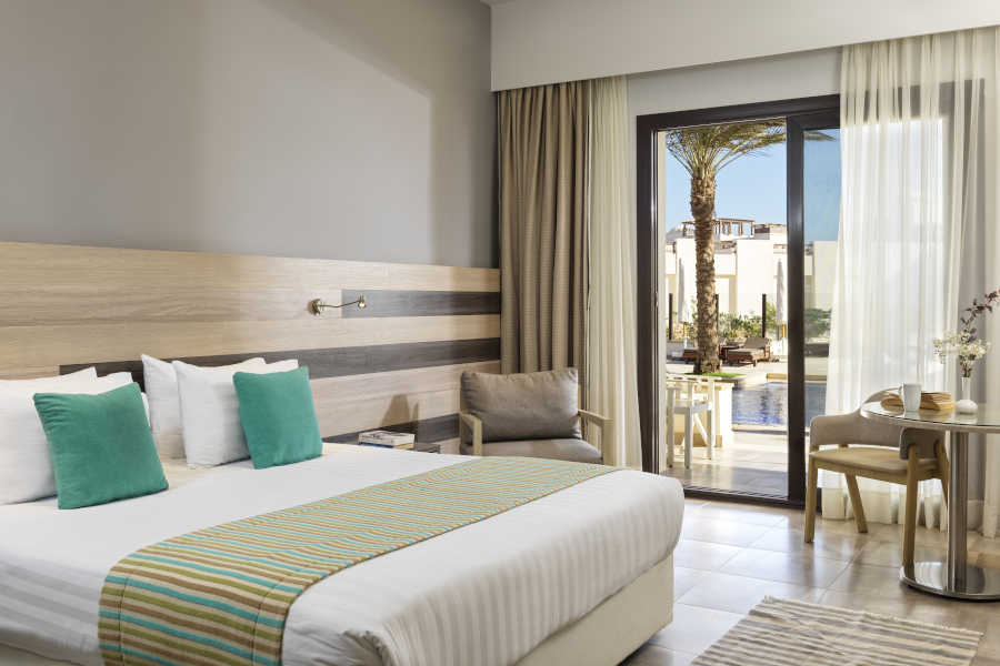 The king sized bedroom at Ancient Sands Resort El Gouna with a glass door to the pool and a beige theme for the decoration