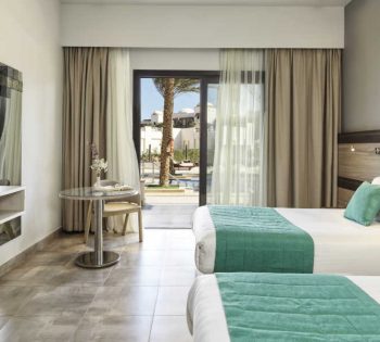 The twin bed of deluxe room at Ancient Sands Resort in El Gouna with a small coffee table and a glass wide window with a view to the pool