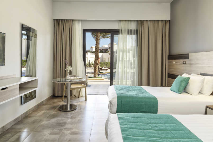 The twin bed of deluxe room at Ancient Sands Resort in El Gouna with a small coffee table and a glass wide window with a view to the pool