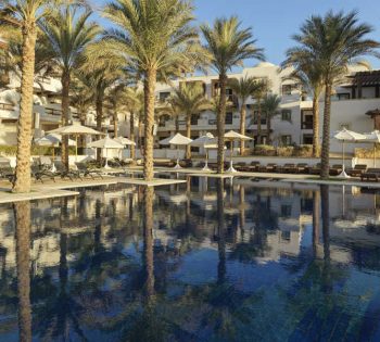 The swimming pool for adults in Ancient Sands Resort surrounded with laid-back sunbeds for spending a relaxing vacation in El Gouna
