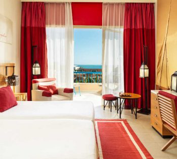 The twin bedroom in red theme with wide glass window to Red Sea view at Club Paradisio four stars hotel in El Gouna
