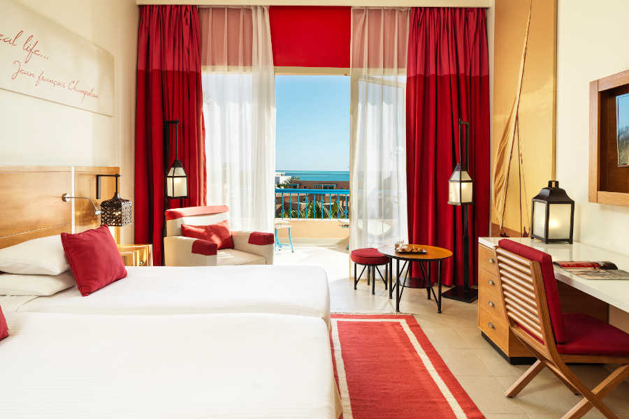 The twin bedroom in red theme with wide glass window to Red Sea view at Club Paradisio four stars hotel in El Gouna