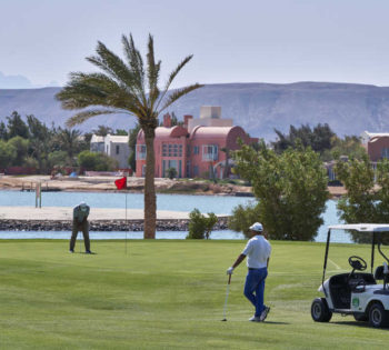 Tee time at Steigenberger Golf Resort in El Gouna with Red Sea lagoon view, golf car and two men