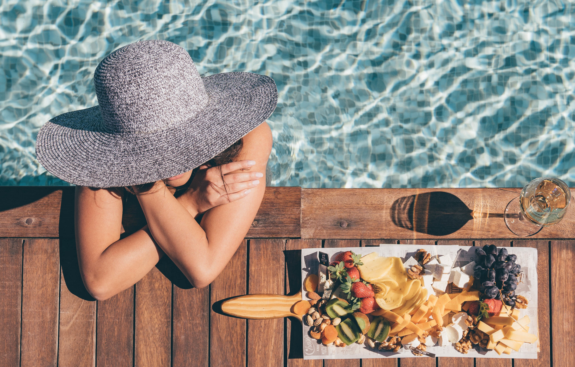 a girl wearing a big hat and chilling in the pool with a serving plate full of food and a glass of wine at cooks club in el gouna