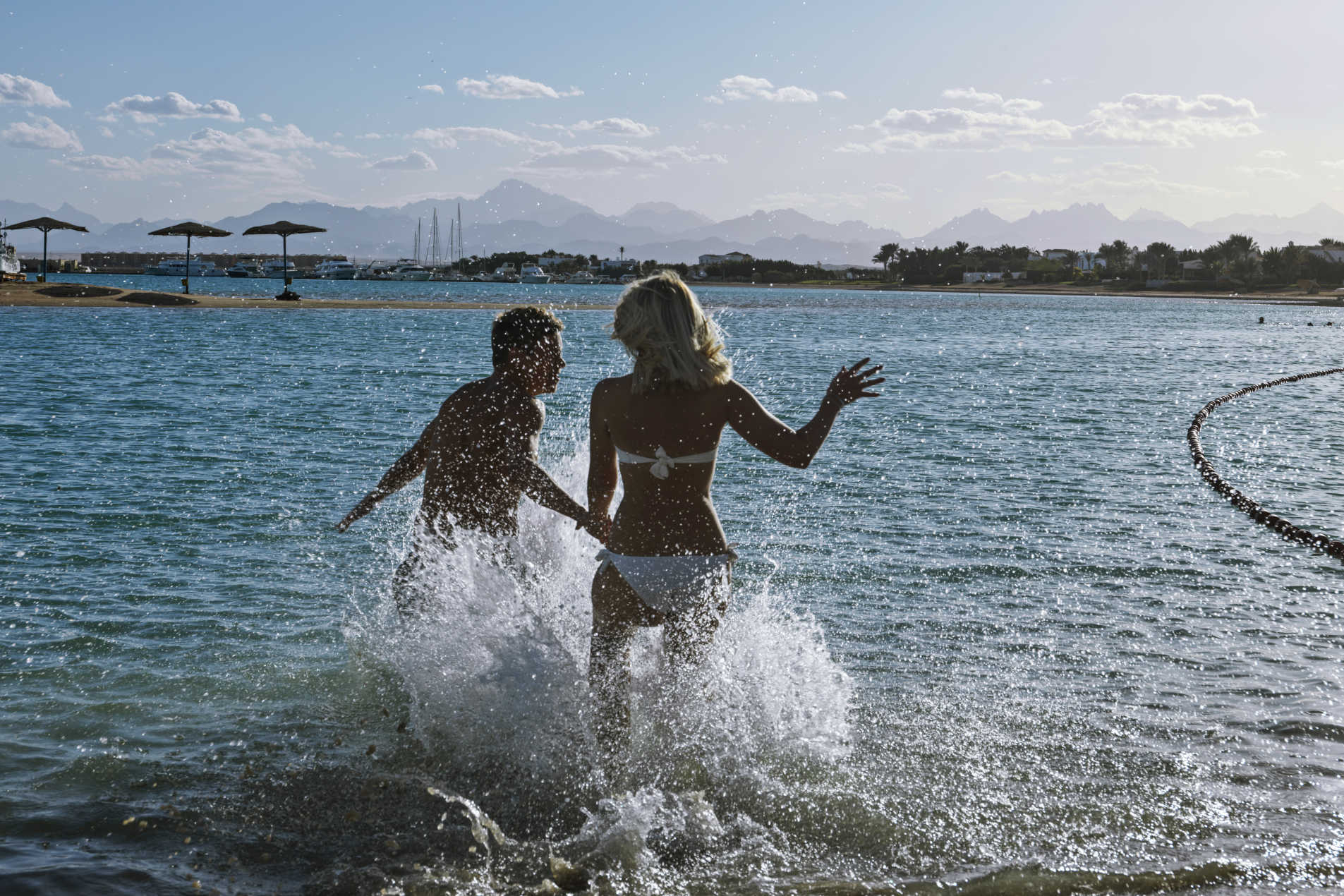 A lady and a guy are holding each other hands and running into the sea at Labranda Hotel Club Paradisio in El Gouna