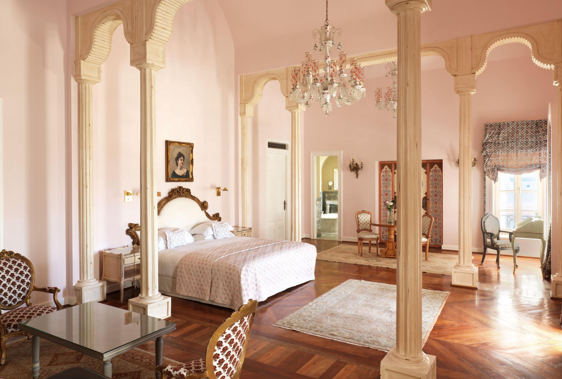 large hotel bedroom with antique pink furniture, wooden floor, bright windows